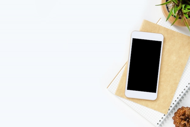 Smartphone with blank screen is on top of white office desk table with supplies.