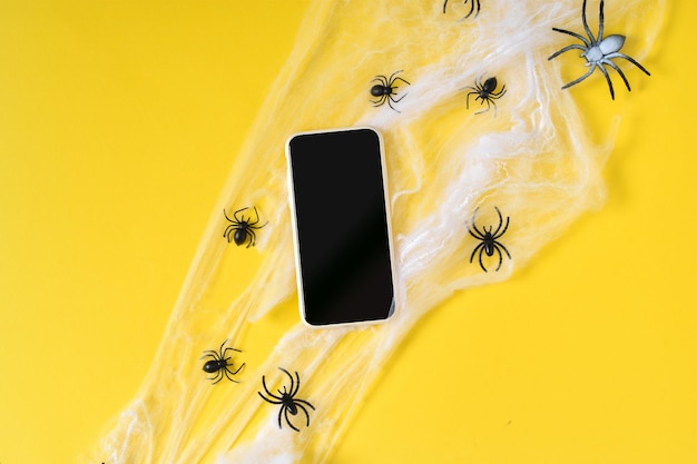 A smartphone with an empty black screen on a yellow background a spider web Happy Halloween