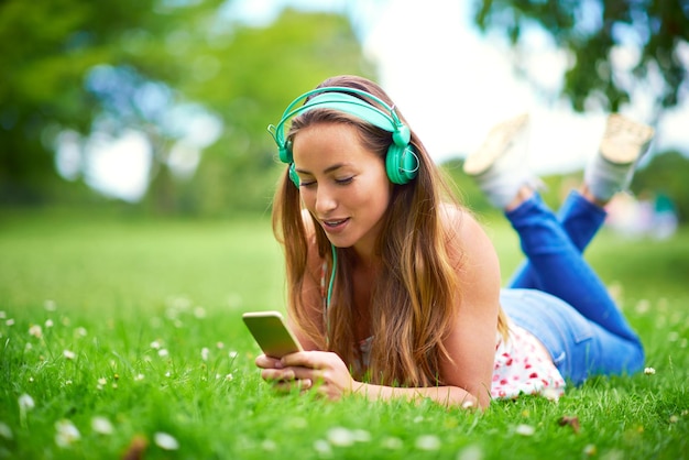 Photo smartphone woman and headphones on grass for music streaming and audio book or podcast college student technology and happy on campus or garden for network online and media for education in park