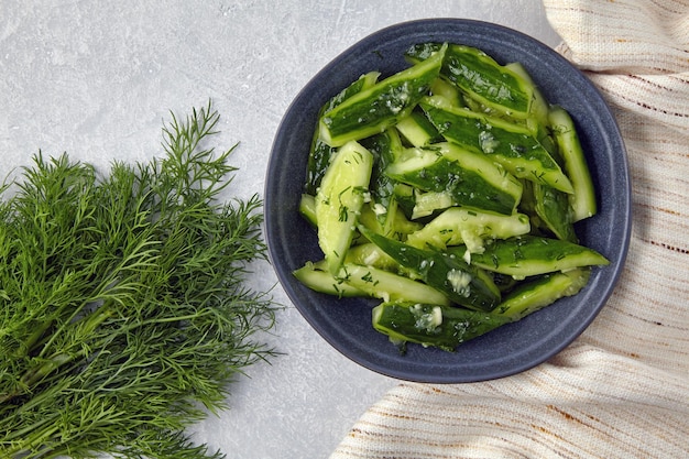 Smashed lightly salted broken cucumbers in a ceramic bowl surrounded by dill and kitchen towel napkin