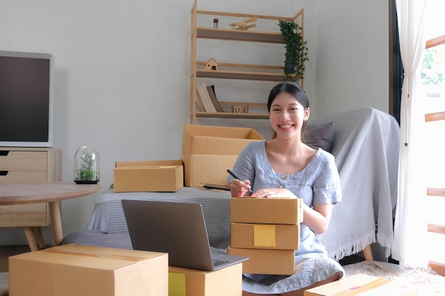 SME entrepreneur Small business entrepreneurs Online selling ideasHappy Young Asian business owner work on computer and a boxs at homedelivery SME procurement package box deliver to customers