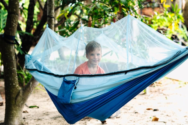 Smile child boy lie rest hammock with mosquito net Happy childhood daydream Look at from laughing portrait