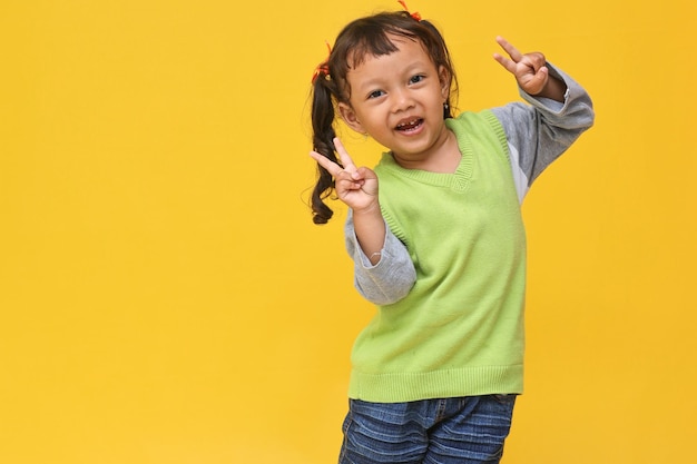 Smile cute of Asian little girl show vsign over yellow background with copy space