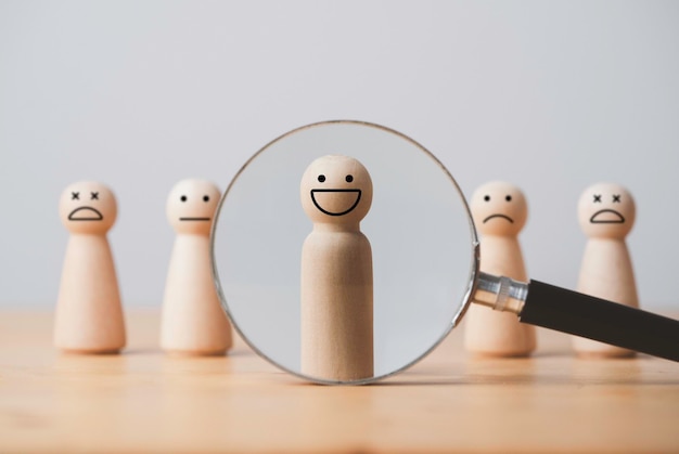 Smile face of wooden figure inside of magnifier glass among sad face for customer focus and relation management excellent evaluation after client use product and service concept