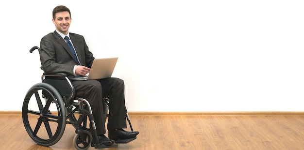 The smile man in the wheelchair works with a laptop on a white wall background