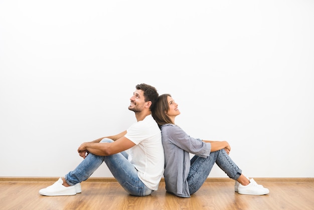 The smile man and woman sit on the background of the empty wall