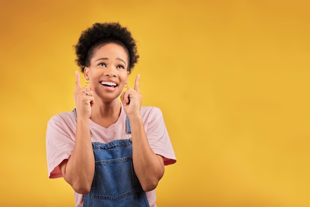 Smile pointing and mockup with a black woman on a yellow background in studio for advertising or marketing Sale presentation or information with a happy young female brand ambassador showing space