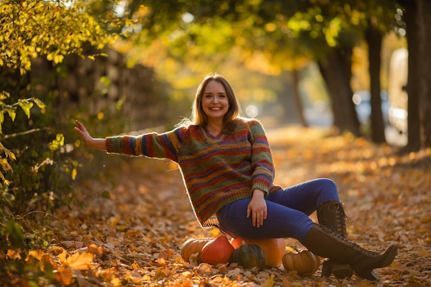 Smile woman sitting on the pumpkin on the autumanl maple leaves