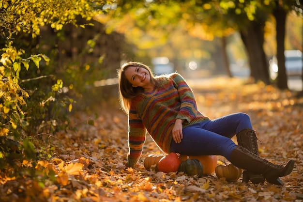 Smile woman sitting on the pumpkin on the autumanl maple leaves