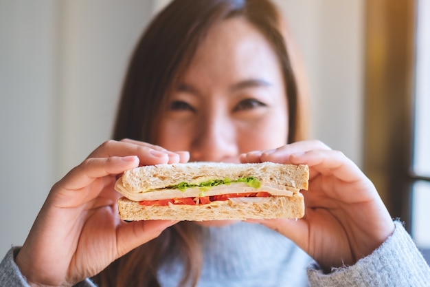 A smiley beautiful woman holding a piece of whole wheat sandwich cover her face