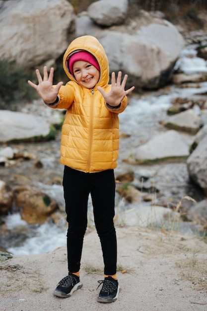 Smiley little girl in a yellow jacket over a blurred mountain nature landscape