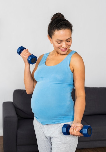 Smiley pregnant woman at home training with weights