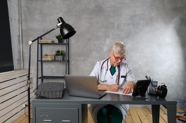 Smiling 60s middle aged female doctor looking at camera. Happy mature elegant old lady posing at hospital.