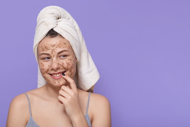 Smiling adorable female posing with cosmetic mask isolated on lilac, looking aside with flirting facial expression