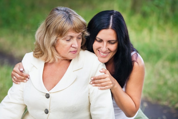 Smiling adult daughter hugs an elderly mother outdoors in a park