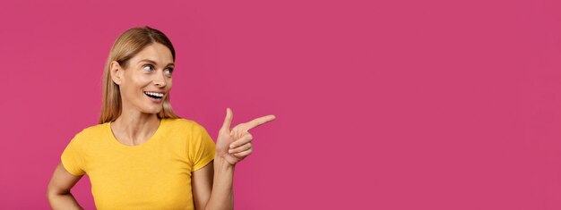 Photo smiling adult european woman with open mouth pointing finger at empty space