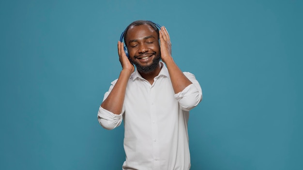 Smiling adult using headphones to listen to mp3 radio music, having fun with creative sound in studio. Energetic cheerful person enjoying audio headset songs, feeling joyful and funky.