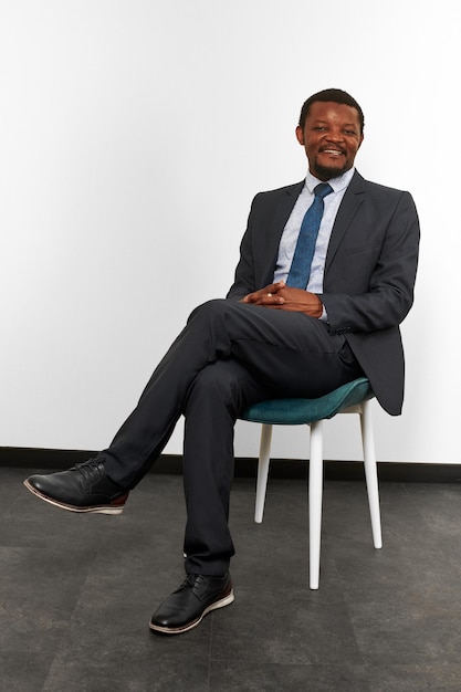 Smiling african american black man in business suit sitting on chair with crossed fingers