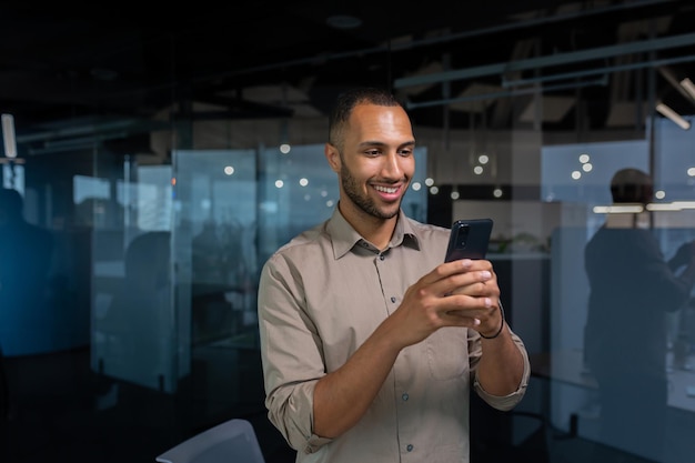 Smiling african american businessman inside office in shirt using phone man typing message and