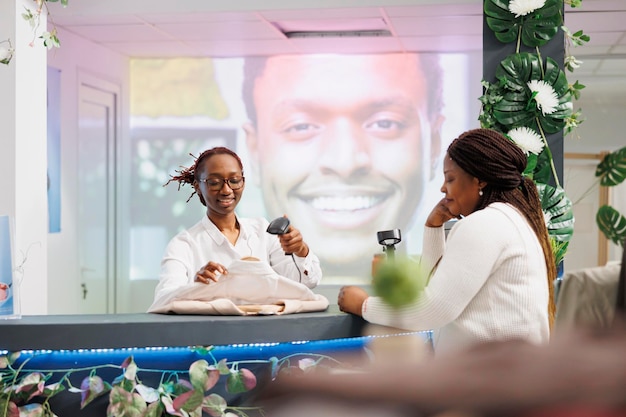 Smiling african american cashier scanning customer clothes at cash register. Woman standing at counter desk, waiting to pay for purchase while employee using pos terminal and scanner