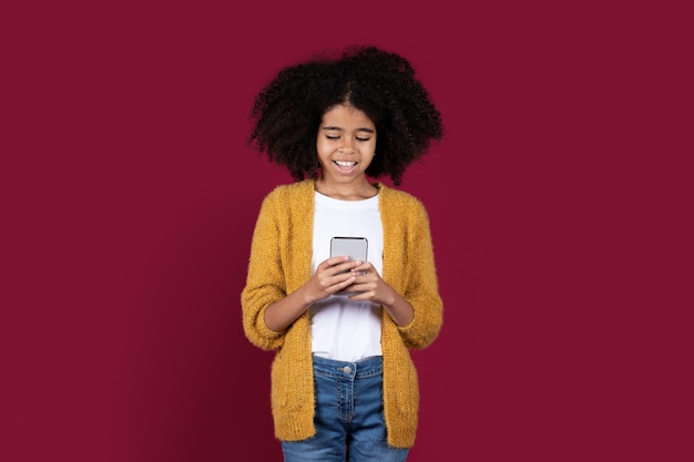 Smiling african american girl using cell phone studio background