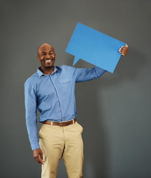 Smiling african american male voter holding a copyspace board sign on public opinion message Casual and positive man holding a social media speech bubble or communication icon for news poll idea