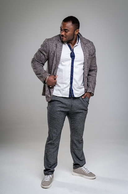 Smiling african american man posing with one arm in pocket and holding stylish jacket. Attractive business man in fashionable grey suit and black tie looking away. Full-lenght photo.