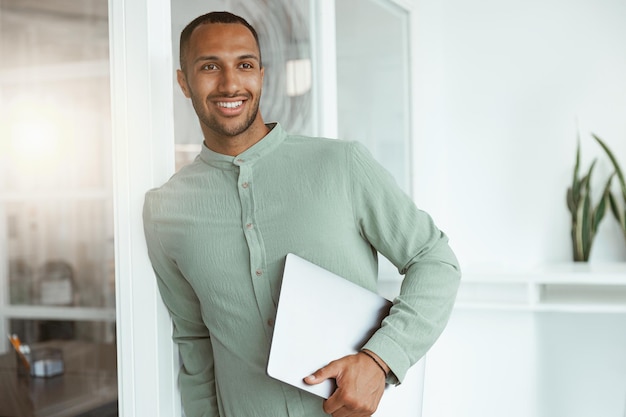 Smiling african businessman holding laptop while standing in cozy office and looking side