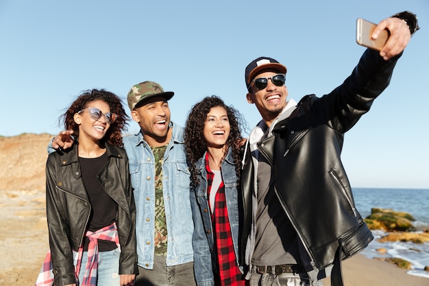 Smiling african friends walking outdoors on the beach make selfie