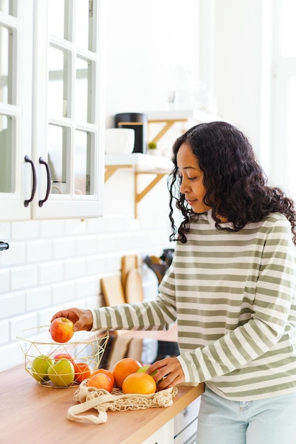 Smiling africanamerican female choosing healthy snack while sorting apples in kitchen