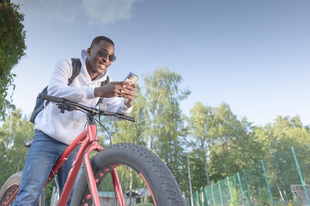 A smiling AfricanAmerican man with a phone in his hands and a bicycle Sports and recreation