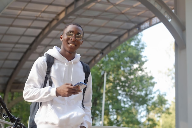 A smiling AfricanAmerican man with a phone in his hands in a public park Sports and recreation