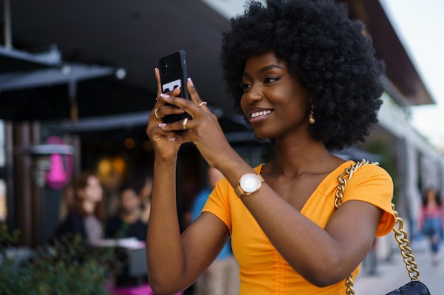 Smiling afroamerican woman holding mobile phone while walking in the street