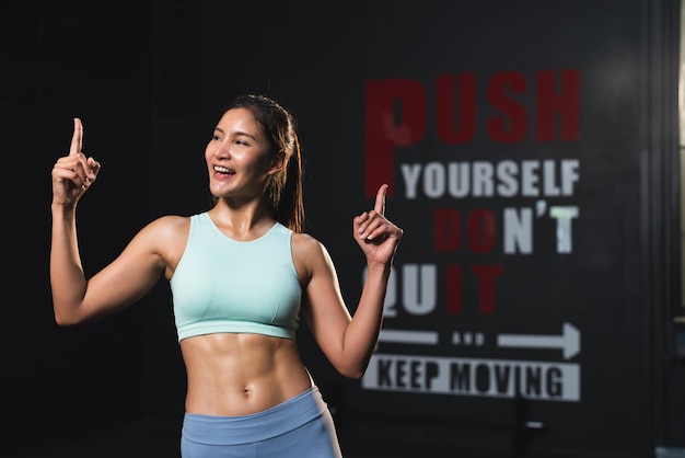 Smiling Asian athlete woman in sportswear slim muscular body posing action after exercise in gym