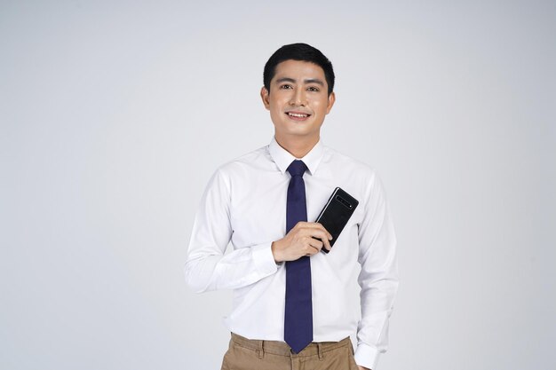 Smiling asian business man standing isolated over gray background using mobile phone