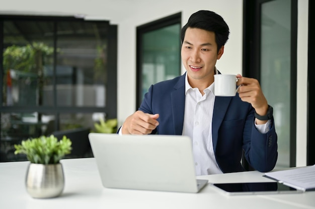 Smiling Asian businessman working on his business task in laptop computer at his desk