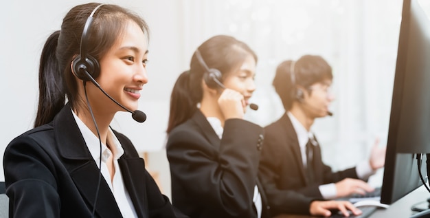 Smiling Asian businesswoman consultant wearing a microphone headset of customer support phone operator at the workplace.