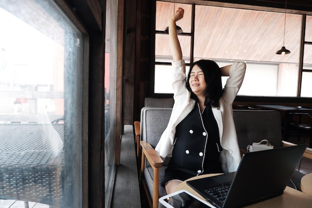 Smiling Asian businesswoman is stretch lazily at workplace in office or relaxing at coffee shop