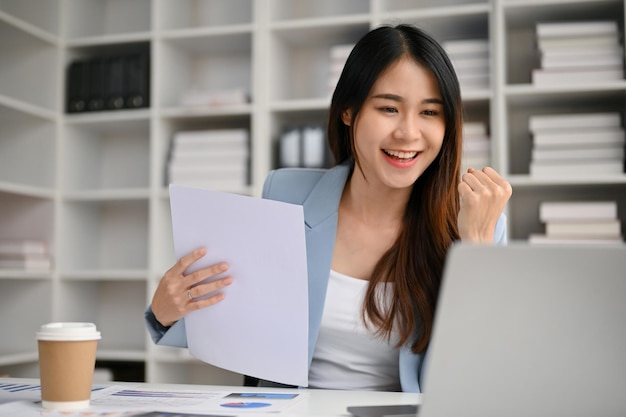 Smiling Asian businesswoman looking at her laptop screen celebrating her project success