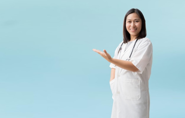 Smiling asian female doctor medical professional holding something in empty hand isolated on blue background with Clipping paths for design work empty free space