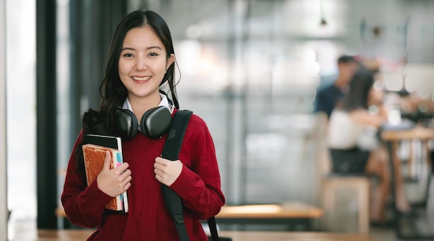 Smiling asian female student holding books standing in classroom