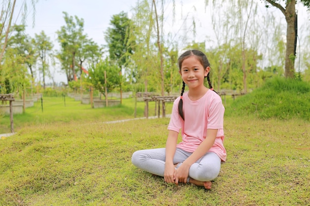 Smiling Asian girl child looking camera while sitting on lawn in the garden