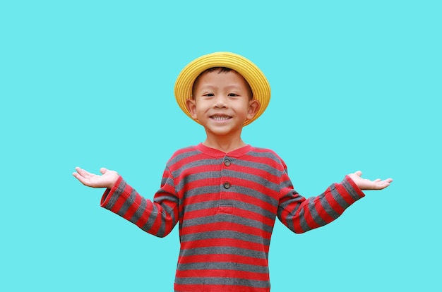 Smiling Asian little boy wearing yellow straw hat standing and open wide arms with looking camera isolated on cyan background Image with Clipping path