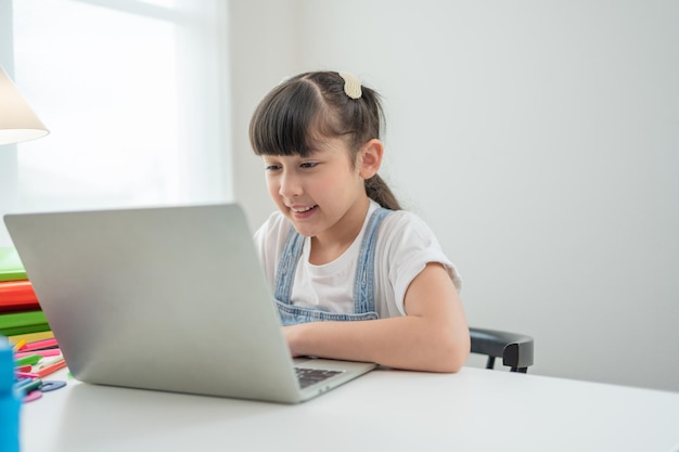 Smiling Asian little girl using laptop doing homeworkChild study online on computer at home