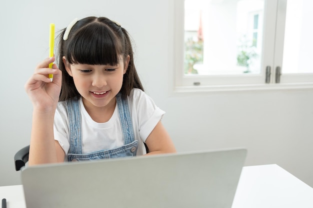 Smiling Asian little girl using laptop doing homeworkChild study online on computer at home