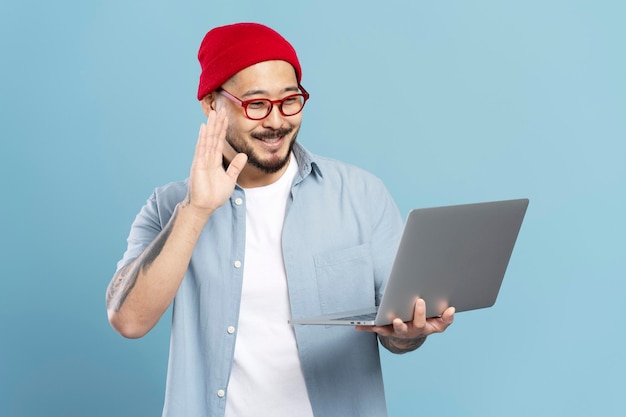 Smiling asian man freelancer holding laptop waving hand having video call