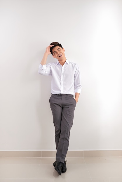 Smiling Asian man in pants and shirt standing near blank wall. Concept of businessman. Mock up