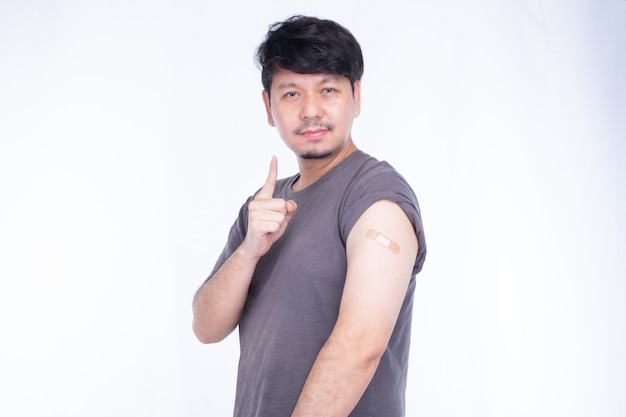 Smiling Asian man showing  shoulder with bandage after getting vaccination immunization, show one finger for first immunization vaccine isolated on white background