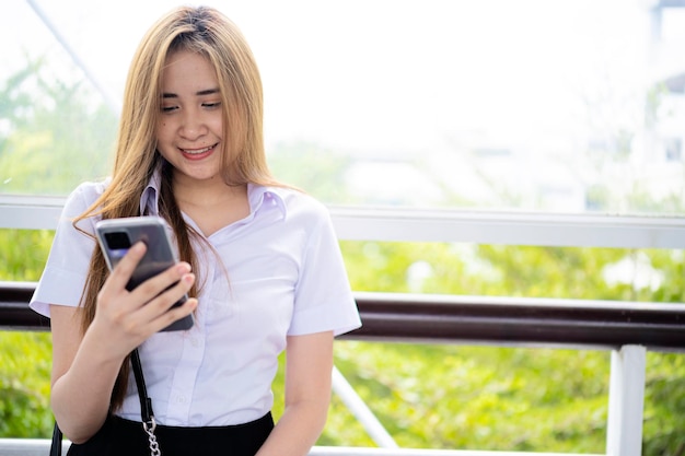 Smiling Asian manager in formalwear texting with friend on smartphone