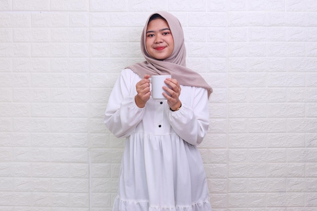 Smiling Asian Muslim woman holds white mug glass drink at iftar time